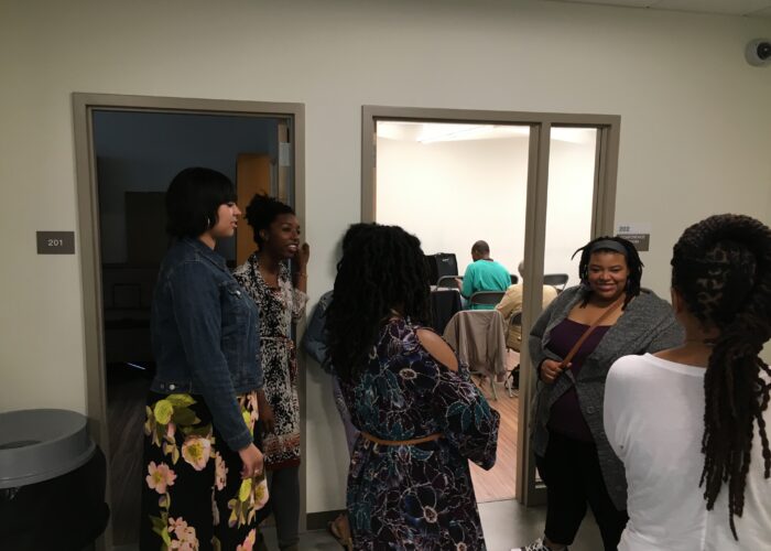 5 women standing and talking outside a room